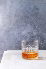 Glass of scotch whiskey standing on white marble table with grey wall at background. Alcohol drink.