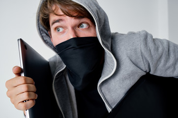 a masked man holds a laptop in his hand