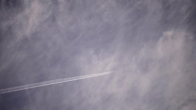 Footage, using a telephoto lens of an airplane flying high in the clouds.