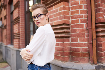 beautiful woman with short hair and glasses stands near a brick building
