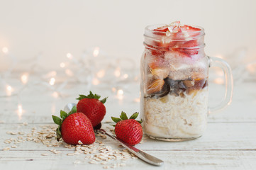 Easy breakfast recipe: overnight oats with strawberry, dried fruits and coconut milk. Healthy pudding in a glass jar served with fresh berries and spoon on wooden table