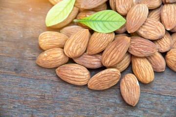 close up of almonds grain roast on wood background with green leaves