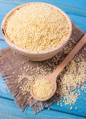 Organic millet seeds in a ceramic bowl on blue wooden table.