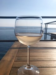 Glass of Rose wine sitting on a wooden table with the sea in the background, taken on a summer's day in Italy. 