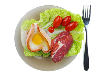 Fried egg, sausage, ham, pickled tomatoes and lettuce leaf on glass plate