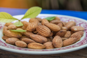 close up of almonds grain roast on wood background with green leaves