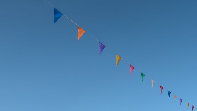 Guirnalda con Banderines de colores en forma de tri&aacute;ngulo colgados en una cuerda con el cielo azul de fondo