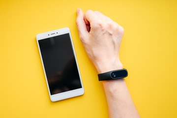 Woman hand with fitness tracker and smartphone on a yellow background