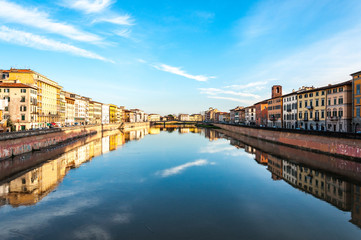 Fototapeta na wymiar Beautiful river in the central part of Pisa surrounded with small houses reflecting in the water with blue sky on the background
