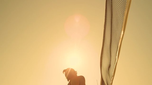 SUN FLARE, SLOW MOTION, LOW ANGLE, CLOSE UP: Female beach volleyball player fails to score a point at sunrise as she spikes the ball into the net. Volleyball athlete strikes the ball into the net.