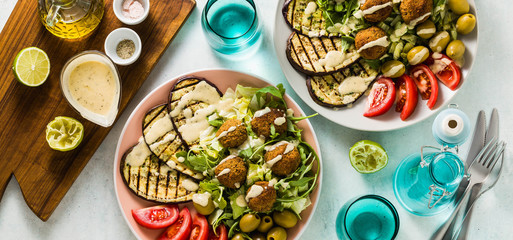 banner of an appetizing dinner or lunch from a salad with tomatoes, grilled eggplants and legume falafel with sesame tahini dressing. Vegan healthy food for the whole family
