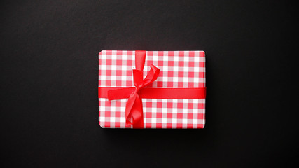 Fototapeta na wymiar Gift box wrapped with red checkered pattern christmas paper with red bow on black table, top view