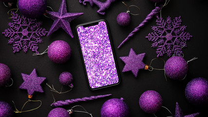 Christmas purple collection, balls and decorative ornaments with modern smarphone in the middle on black background. Top view.