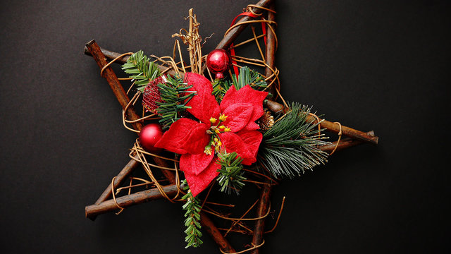 Christmas wreath with dry twigs, pine branches, red balls and poinsettia flower on wooden star shaped decoration isolated on black background. Flat lay. Top view.