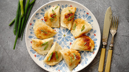 Fried dumplings with meat filling sprinkled with fresh chive on a blue colorful plate. Top view on gray stone background