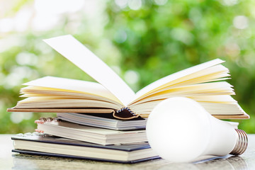Stack of opened books with LED lamp against blurred natural green background for education concept