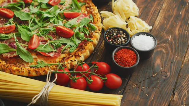 Italian food background with pizza, raw pasta, spices, herbs, wine, and vegetables on wooden table