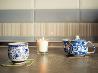 Side view cup, kettle of tea and candle on grey wooden table.