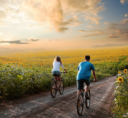 Teen couple riding bike in sunflower field