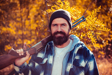 Bearded hunter man holding gun and walking in forest. Hunter with shotgun gun on hunt. Autumn...
