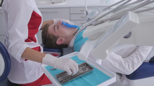 Dentist is treating patient in modern dental office. The operation is carried out using cofferdam.