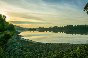 Fototapeta premium Morning view of sun dawn over a lake, reflection in water of blue, pink and yellow sky, dark lake shore in foreground, autumn landscape
