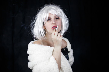 Attractive young woman in costume smoking cigar and looking at camera while standing on black background 