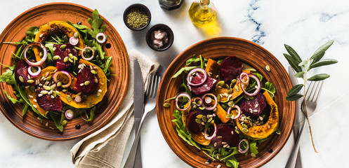 banner of warm salad of baked pumpkin and beets with arugula and seeds on a marble table. healthy...