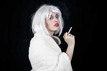 Obraz premium Attractive young woman in costume smoking cigar and looking at camera while standing on black background 