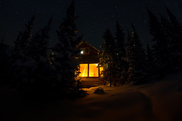 Light from the window of a forest hut under the night sky of the milky way in the winter forest