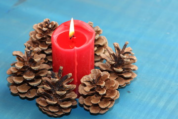Fototapeta na wymiar Red candle and pine cone on blue background.