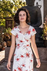 Fototapeta premium Headshot of beautiful young teen dressed in long flower print dress walking along concrete pathl in garden.