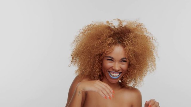 mixed race woman with big curly afro blonde hair hide her smile behind her hands and then show it up
