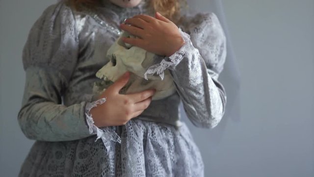 Girl dressed as a dracula bride is holding a one-eyed skull. Gray color range. Day of the dead, hallowen