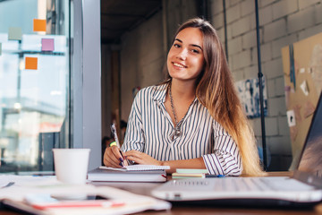 Portrait of smiling female student writing looking at camera sitting at table