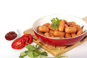 Fried sausages in the red pan and fresh tomato, ketchup, coriander on the wood plate, isolated white background.