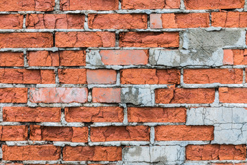 The old building wall of red bricks with cracks, clefts, chips and the parts of plaster