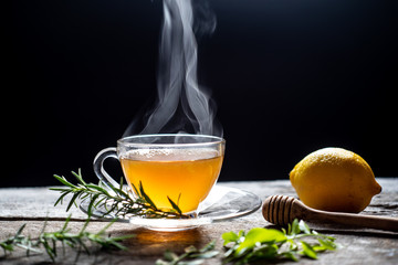 Hot tea in glass cup with steam and lemon .tea leaves and mint herb on wood background