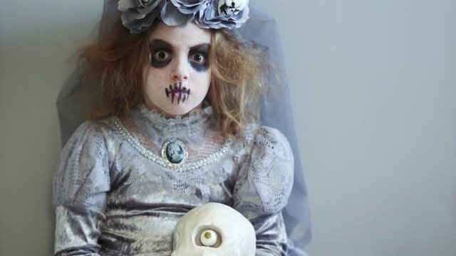 Portrait of a girl dressed as a dracula bride. The child is holding a one-eyed skull. Gray color range. Day of the dead, hallowen