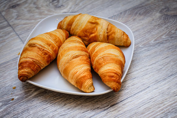 Delicious croissants on a square white plate on a wooden tabletop.