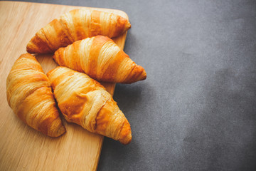 Four croissants on a wooden light cutting board on dark craft paper.