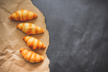Four croissants on brown craft paper on a dark contrasting background.