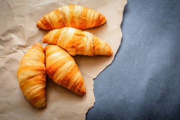 Four croissants on brown craft paper on a dark contrasting background.