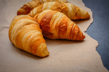 Four croissants on brown craft paper on a dark contrasting background.