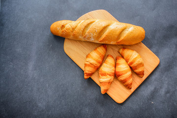 French loaf and four croissants on a wooden cutting board on dark craft paper.