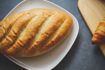 French loaf and four croissants on a wooden cutting board on dark craft paper.