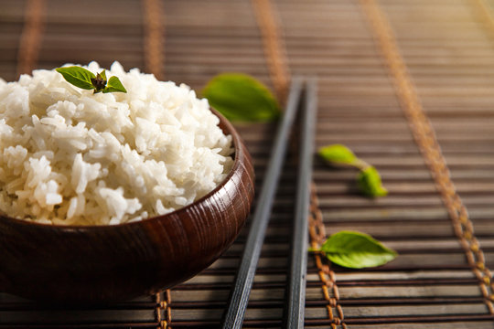 Cooked white rice (Thai Jasmine rice), rice in dark wooden bowl with chopsticks on the wood black bamboo background.