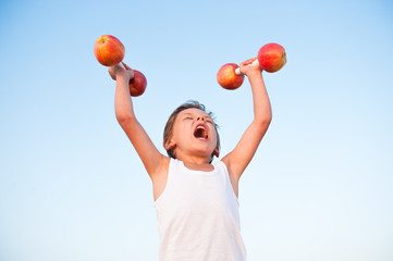 strong healthy kid in white shirt lifting dumbbells made from apples shouting