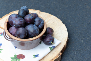 Violet, large, ripe plums on a wooden stand, on a black background