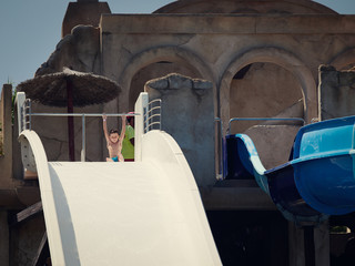 Cute european boy is sitting on the large white water slide. He is going to slide down.